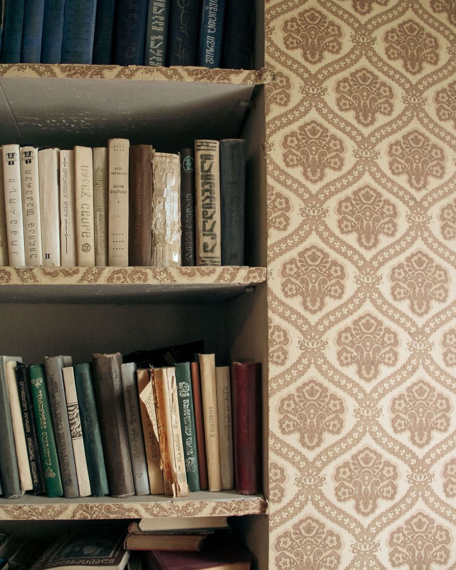 Home library corner with a cream and tan damask wallpaper beside built-in shelves full of old books