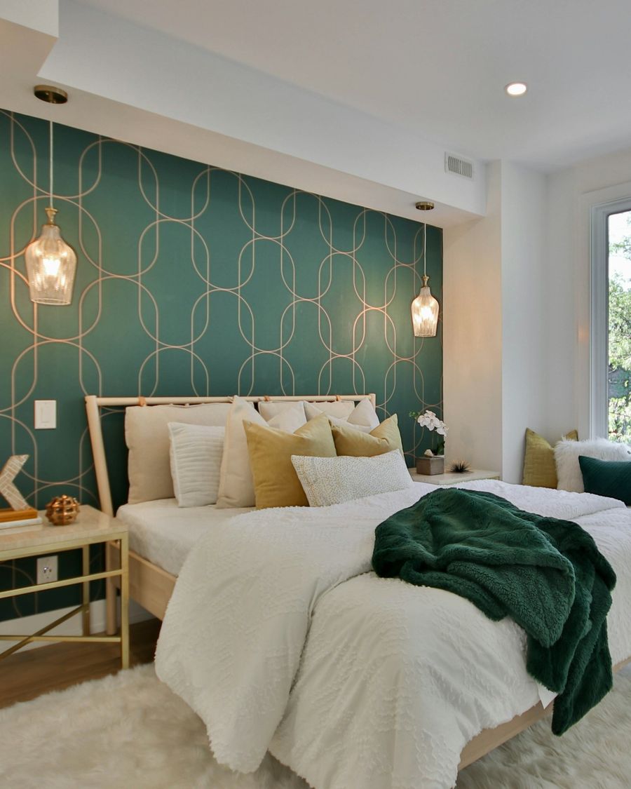 Bedroom with a deep green Art Deco geometric wallpaper on the wall behind a white bed and pendant lamps