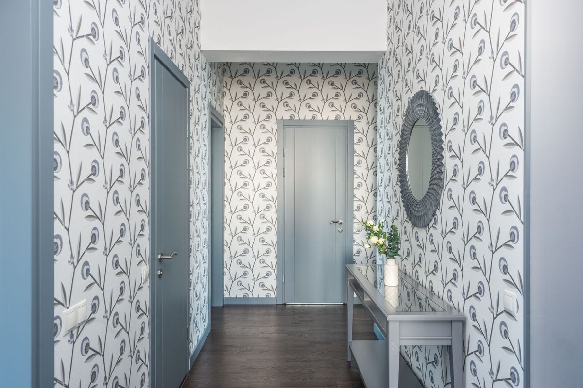 Entry hallway lined with a gray and white trailing-leaf wallpaper, a slim console table, and a round mirror