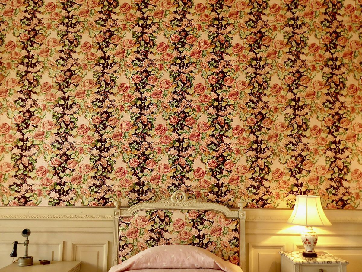 Striped rose-print wallpaper meeting cream wall paneling above an upholstered headboard and a glowing table lamp